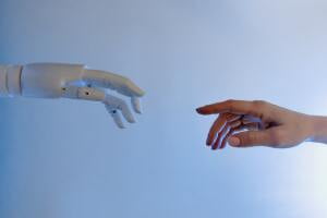 A.I. hand reaching a finger out to touch the finger of a human hand.